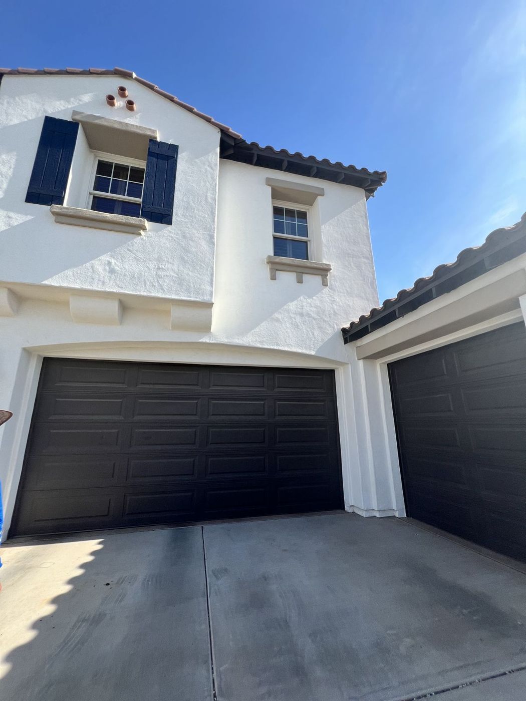 White stucco home repainted with dark garage doors